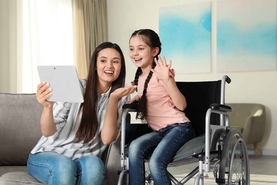 Girl in wheelchair and her mother using video chat on tablet at home
